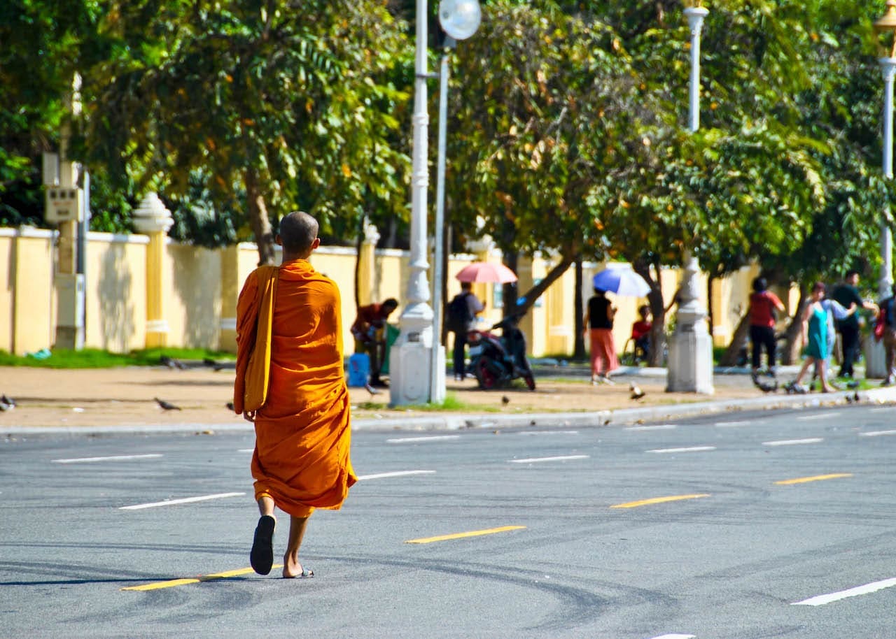 A sole monk wearing a saffron robe walks down an empty four-lane street in Cambodia.