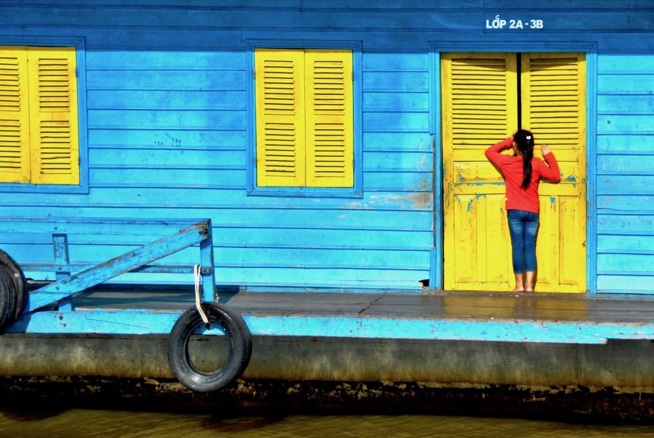 A young girl peeks into a classroom at a bright blue and yellow floating school on Tonlé Sap lake.