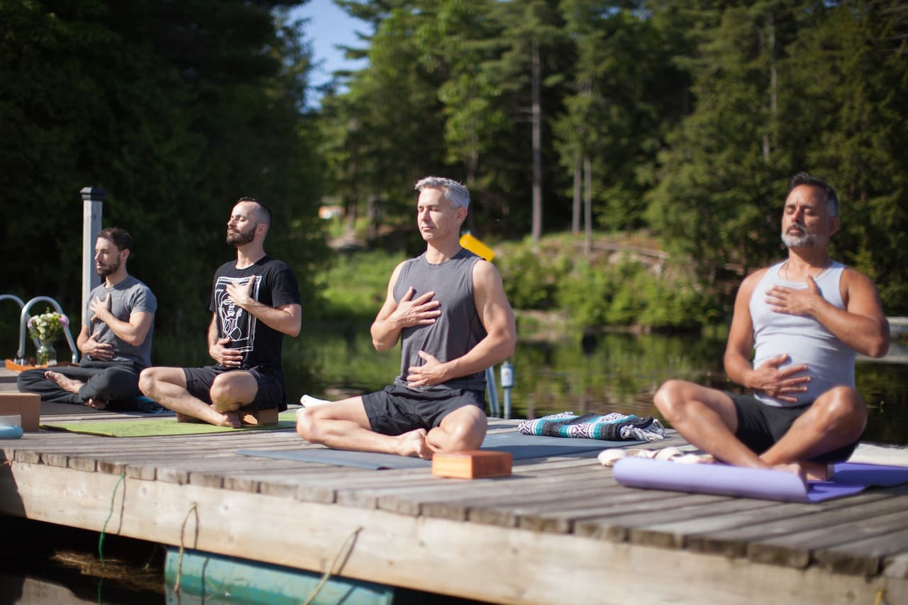 Gay men sit along a dock practicing yoga on a Men's Retreat.