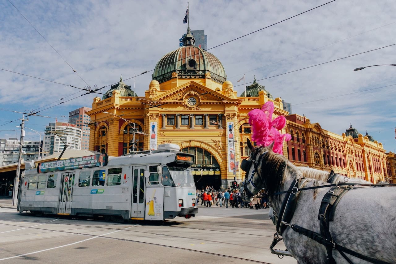 A tram and horse-drawn carriage pass by Flinders Street Railyway in Melbourne.